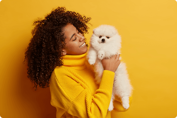 Woman in yellow sweater holding a white Pomeranian puppy
